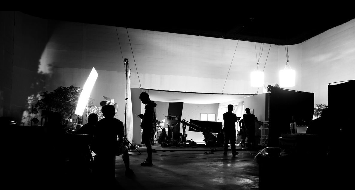 Behind the shooting video production and lighting set for filming which movie crew team working and silhouette shadow of camera and professional equipment in big studio for commercial advertising.